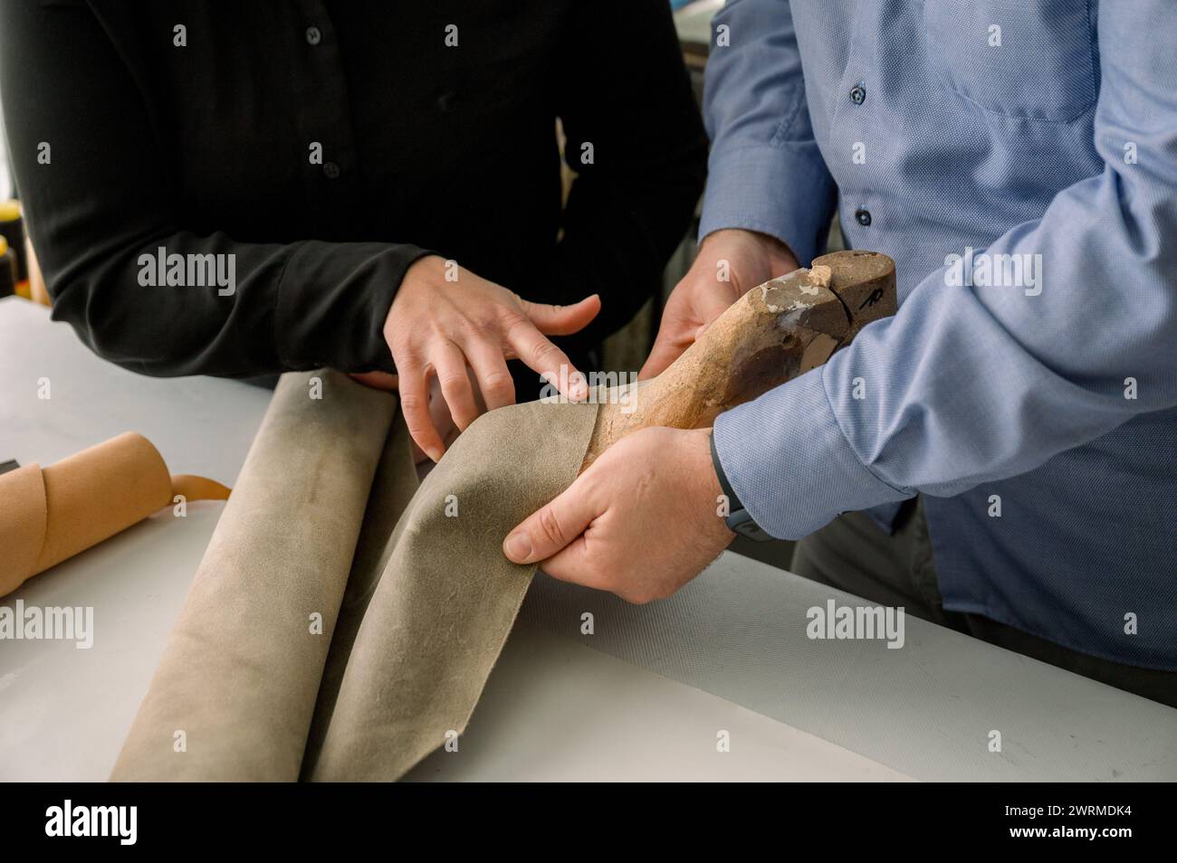 Des artisans recadrés méconnaissables façonnent soigneusement le cuir sur une forme en bois dans un atelier de cordonnerie en Autriche. Banque D'Images