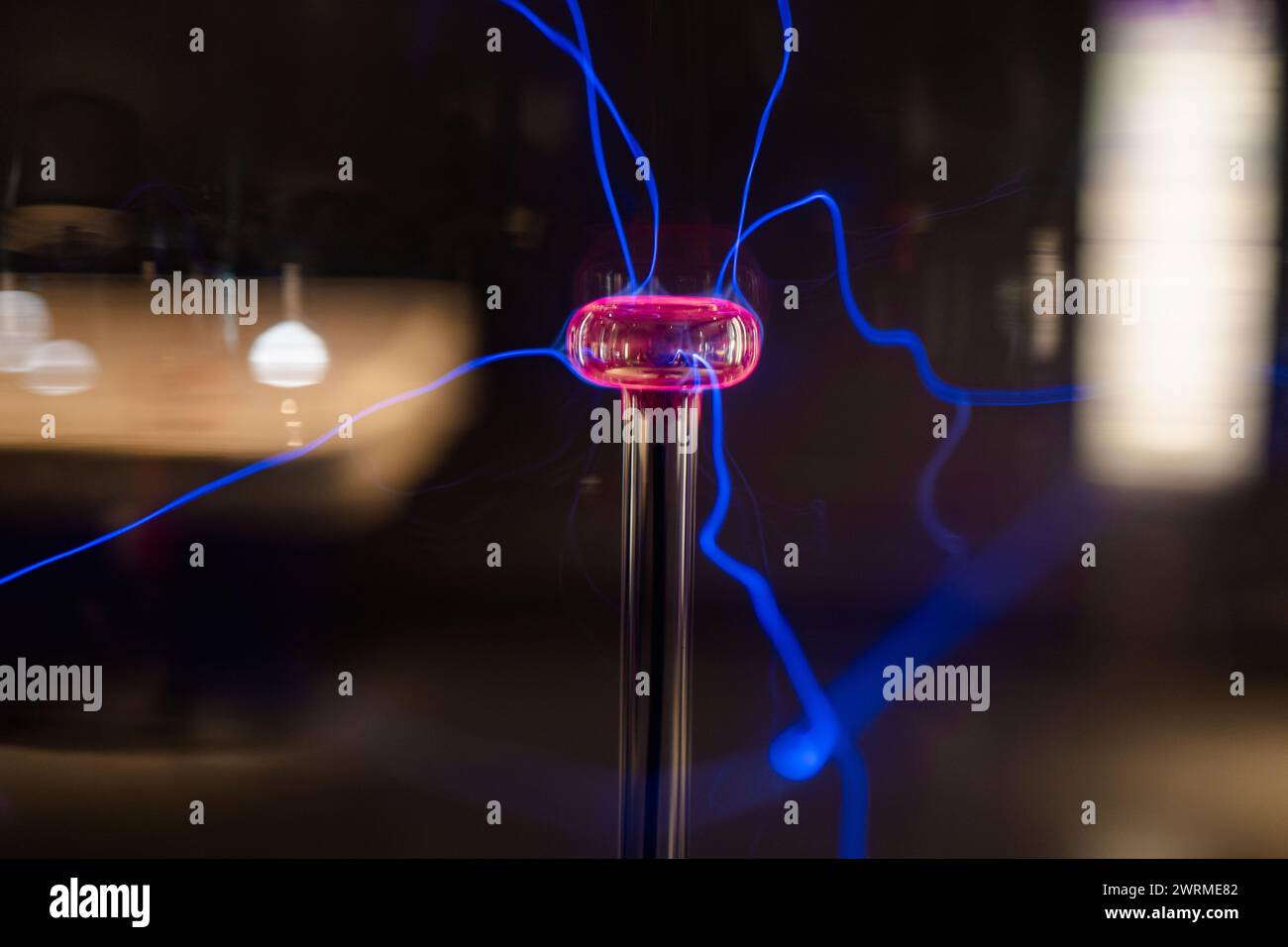 Une boule de plasma éclairant avec des arcs électriques bleus et roses éclatants sur un fond sombre, démontrant les principes de la physique et de l'électricité. Banque D'Images