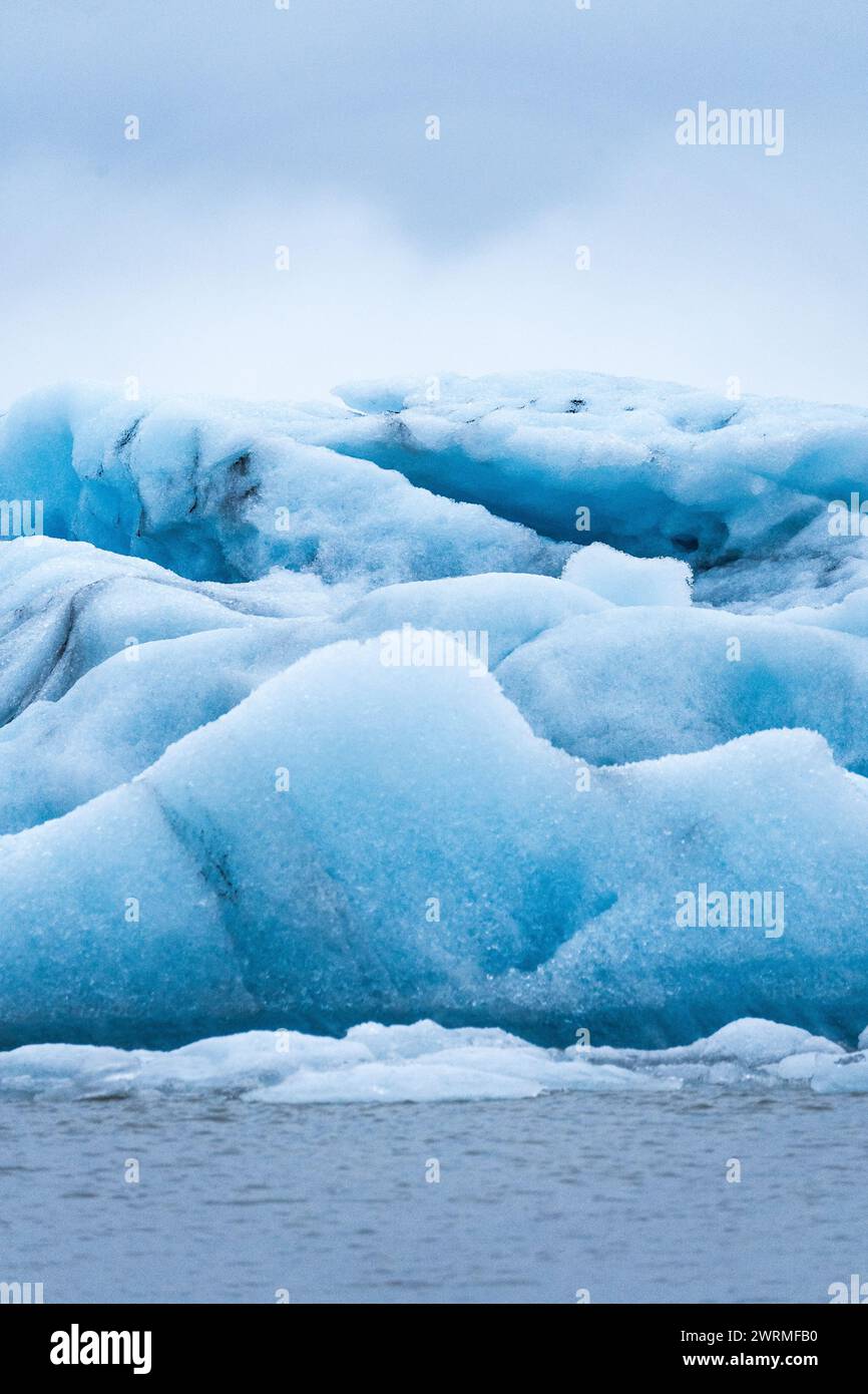 Une image tranquille capturant les nuances bleues subtiles d'un iceberg flottant dans le parc national de Vatnajokull, en Islande, face à un ciel gris et doux Banque D'Images