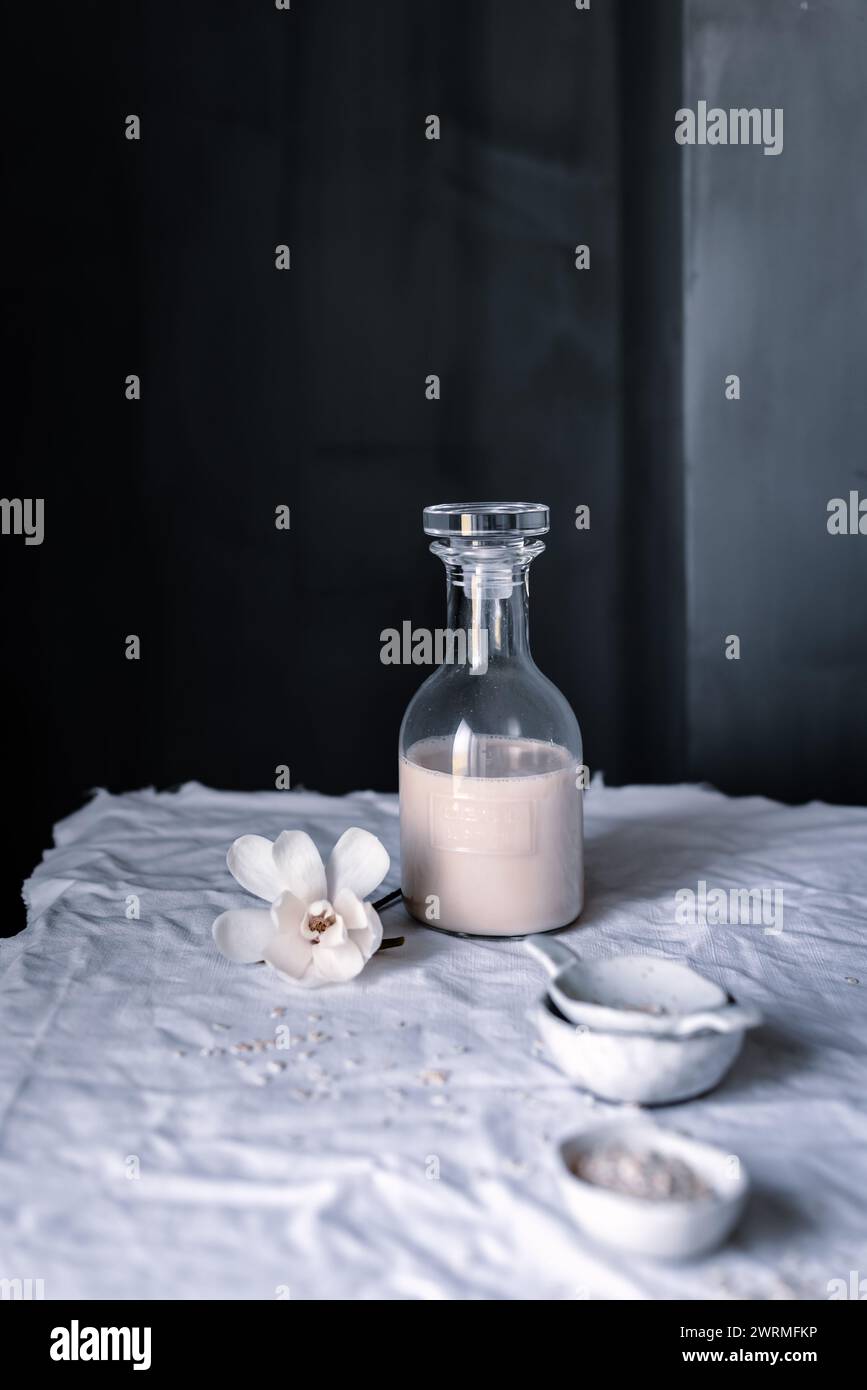 Une composition sereine avec une bouteille en verre de lait d'avoine maison, un accent floral délicat et de l'avoine dispersée, le tout baigné dans une lumière douce et naturelle Banque D'Images