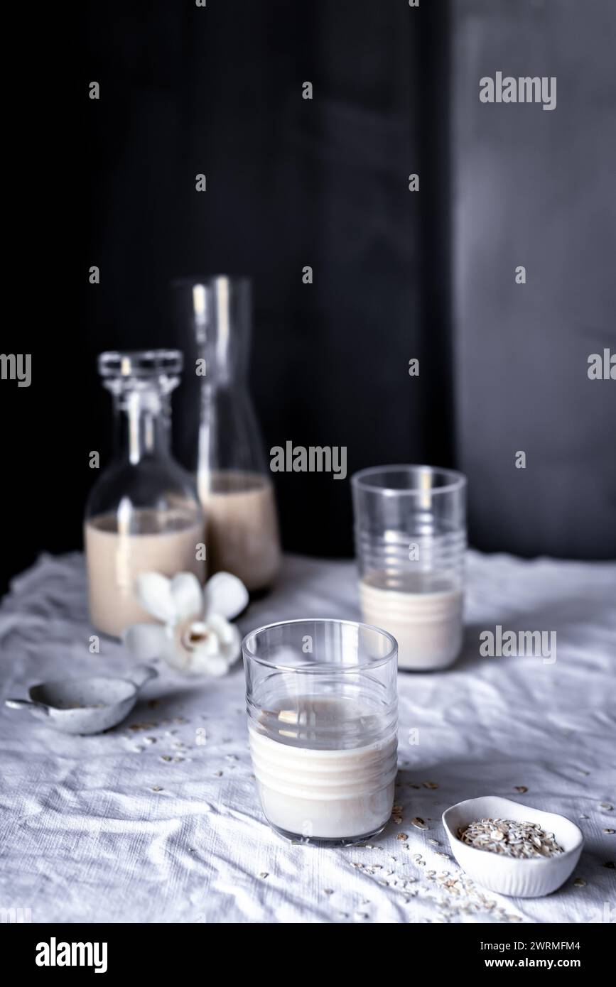 Une scène sereine sur table avec du lait d'avoine fait maison dans des bouteilles en verre et un gobelet, accentuée d'avoine crue et de fleurs d'orchidée Banque D'Images