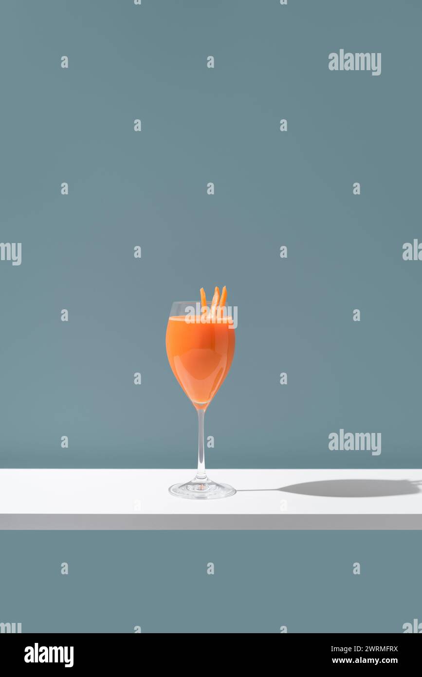 Une image minimaliste mettant en valeur une boisson de couleur orange élégamment présentée dans un verre à vin, ornée de tranches d'orange comme garniture contre un b moelleux Banque D'Images