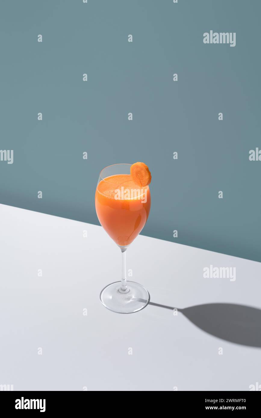 Un verre rafraîchissant de jus d'orange garni d'une tranche, projetant une ombre sur une surface blanche. Banque D'Images