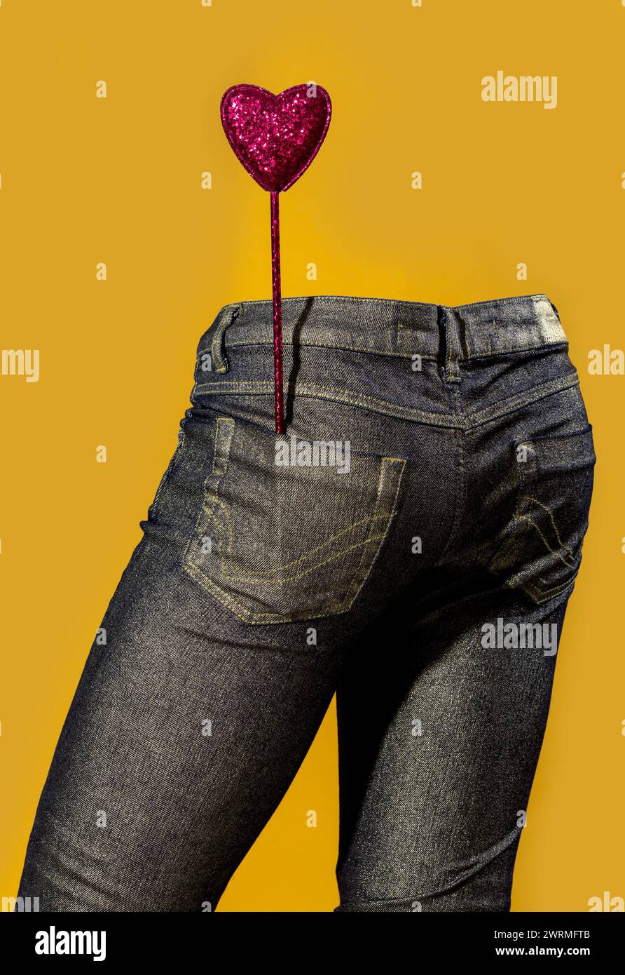 Une sucette rose pailletée en forme de coeur ressort d'une poche de Jean en denim foncé sur un fond jaune vif, présentant un i ludique et vibrant Banque D'Images