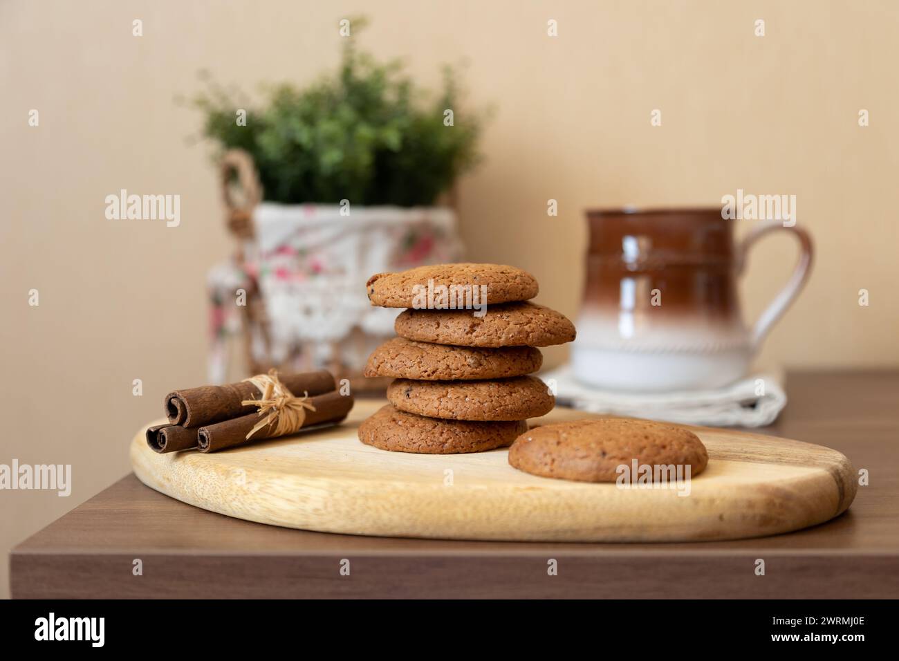 Biscuits aux raisins secs d'avoine sur une planche de bois avec des bâtons de cannelle (Cassia) et une tasse de lait. Pâtisserie traditionnelle maison dans un style rustique. Mise au point sélective Banque D'Images