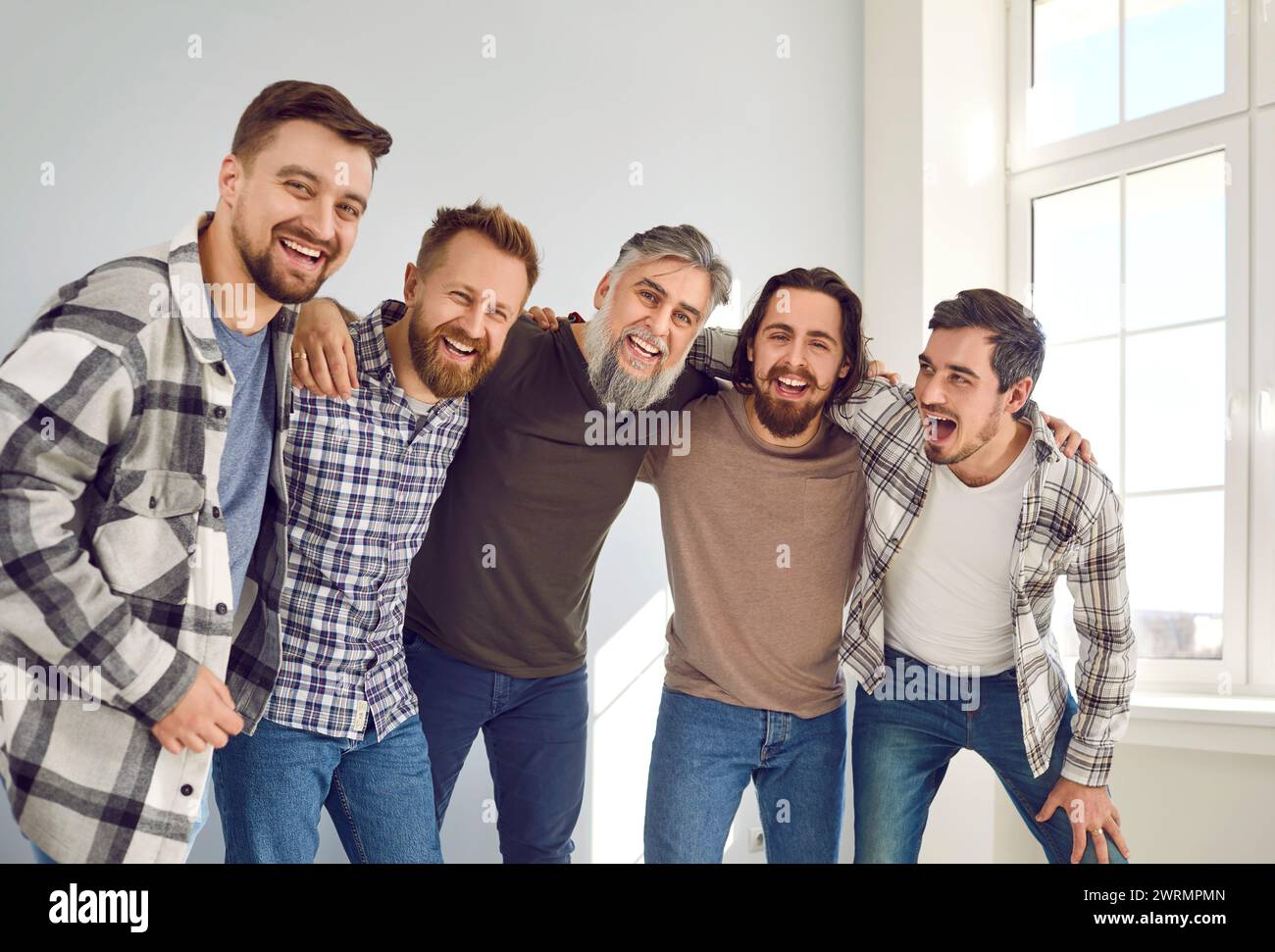 Groupe d'amis masculins heureux et positifs qui s'étreignent, rient et s'amusent ensemble Banque D'Images