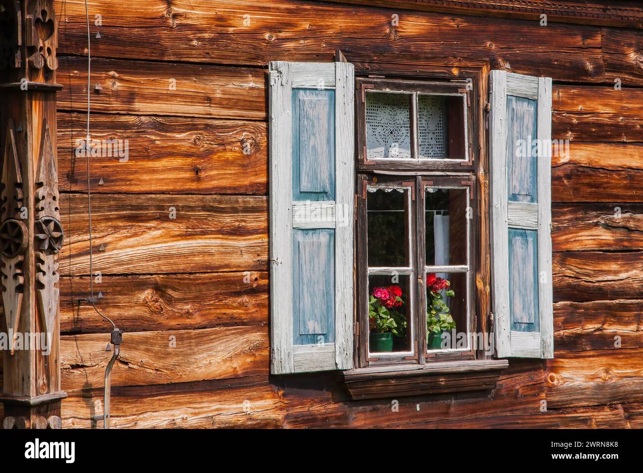 Une fenêtre d'une ancienne maison de campagne avec des volets en bois et des fleurs derrière la vitre Banque D'Images