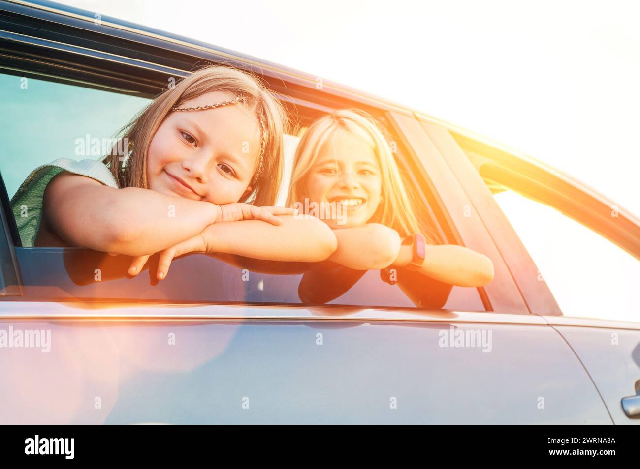 Deux sœurs heureuses regardant par la fenêtre ouverte de la voiture pendant le voyage en voiture. Les filles mignonnes sourient, rient pendant la route jorney. Valeurs familiales, concept de voyage Banque D'Images