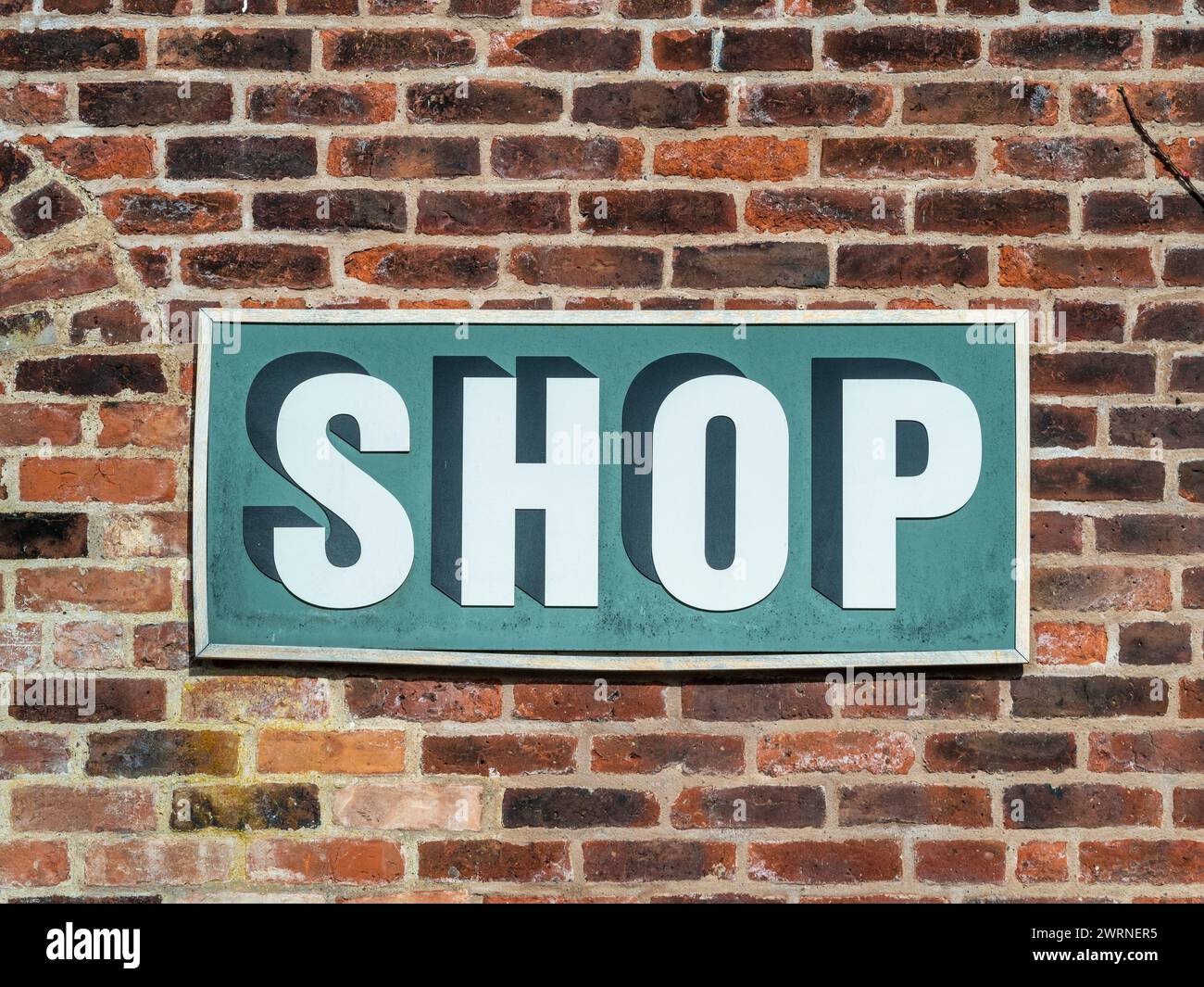 Un panneau en bois monté sur un mur de briques avec le mot «shop» peint à la main dessus. Banque D'Images