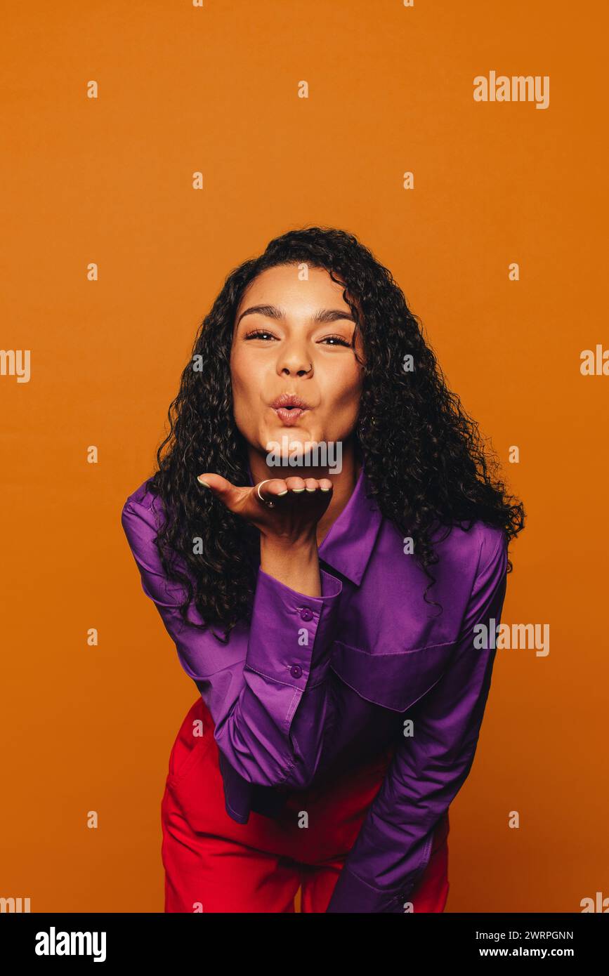 Femme confiante dans une tenue décontractée et colorée sur un fond orange vibrant. Ses cheveux bouclés et son style color block complètent son look tendance et haut Banque D'Images