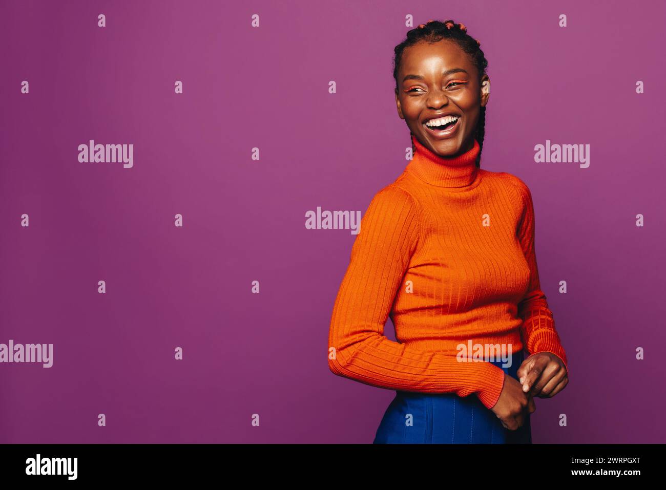 Jeune femme heureuse dans la vingtaine se tient dans un studio, portant des vêtements décontractés et un col polo violet éclatant. Ses élégantes tresses bicolores mettent en valeur son fashi Banque D'Images