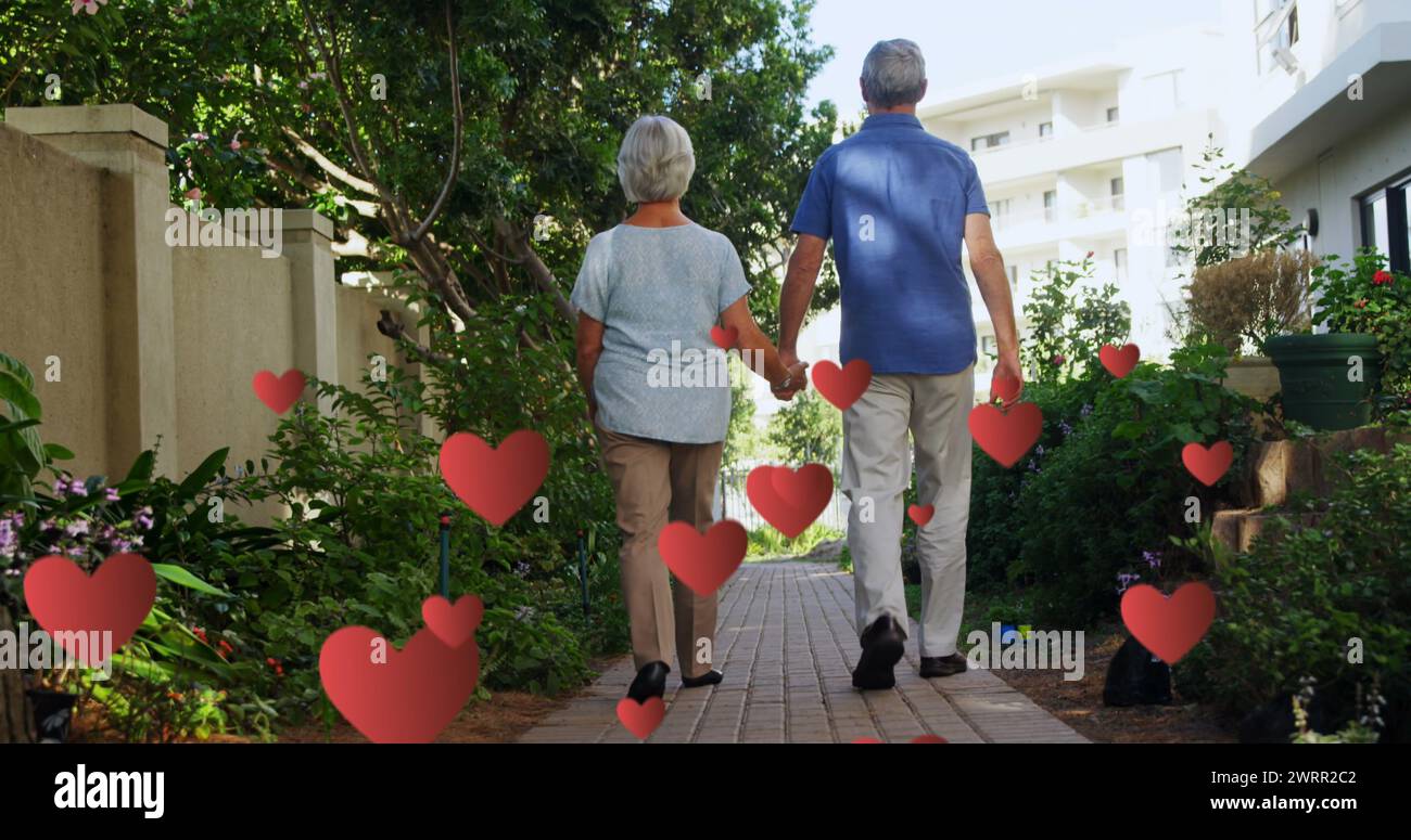 Image de cœurs tombant au-dessus d'un couple de personnes âgées caucasiennes marchant Banque D'Images