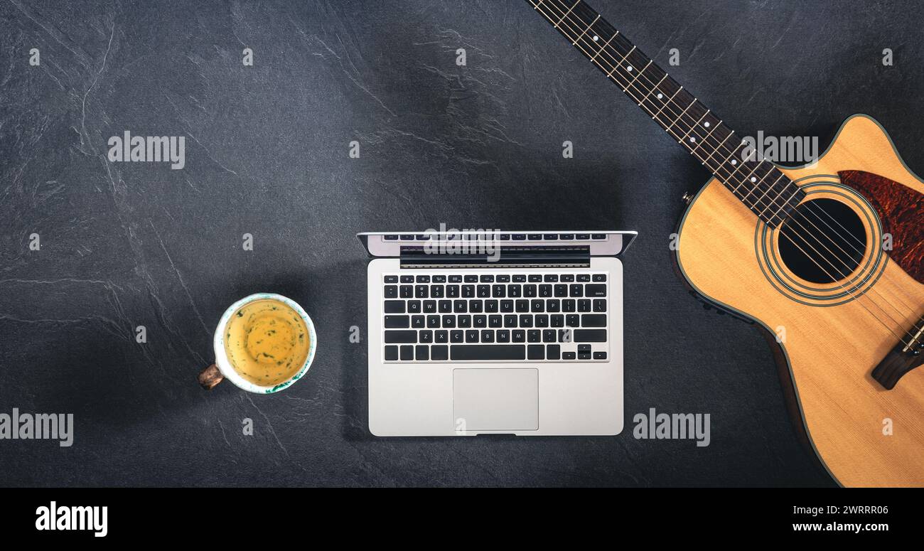 Ordinateur portable, guitare acoustique et une tasse de thé sur fond noir, vue de dessus. Banque D'Images