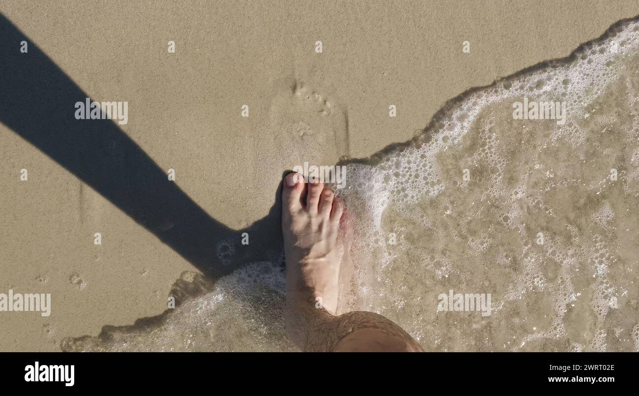 Pieds mâles nus marchant sur le rivage sablonneux avec des vagues. Profiter de l'océan. Liberté et tranquillité. Vacances ou concept de vacances. Photo de haute qualité Banque D'Images