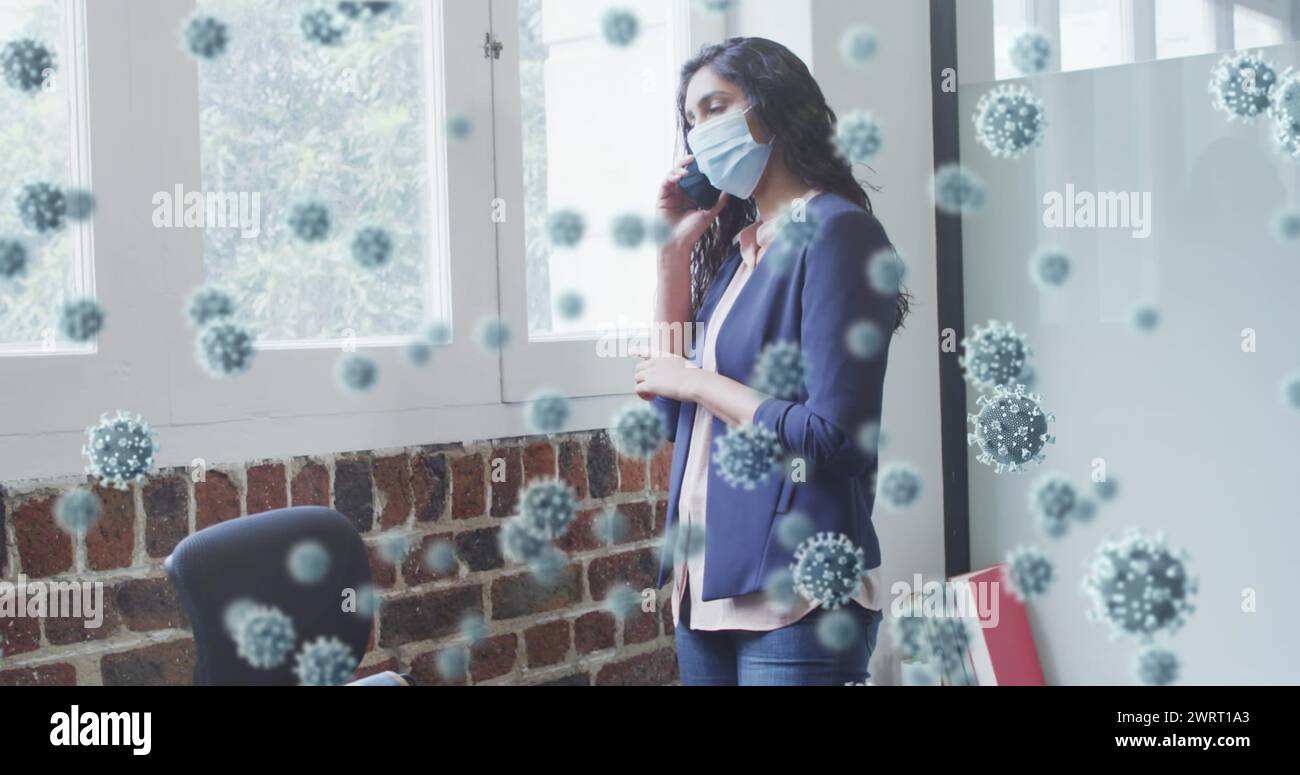 Image de cellules covid 19 flottant au-dessus d'un homme portant un masque facial, en utilisant un smartphone au bureau Banque D'Images