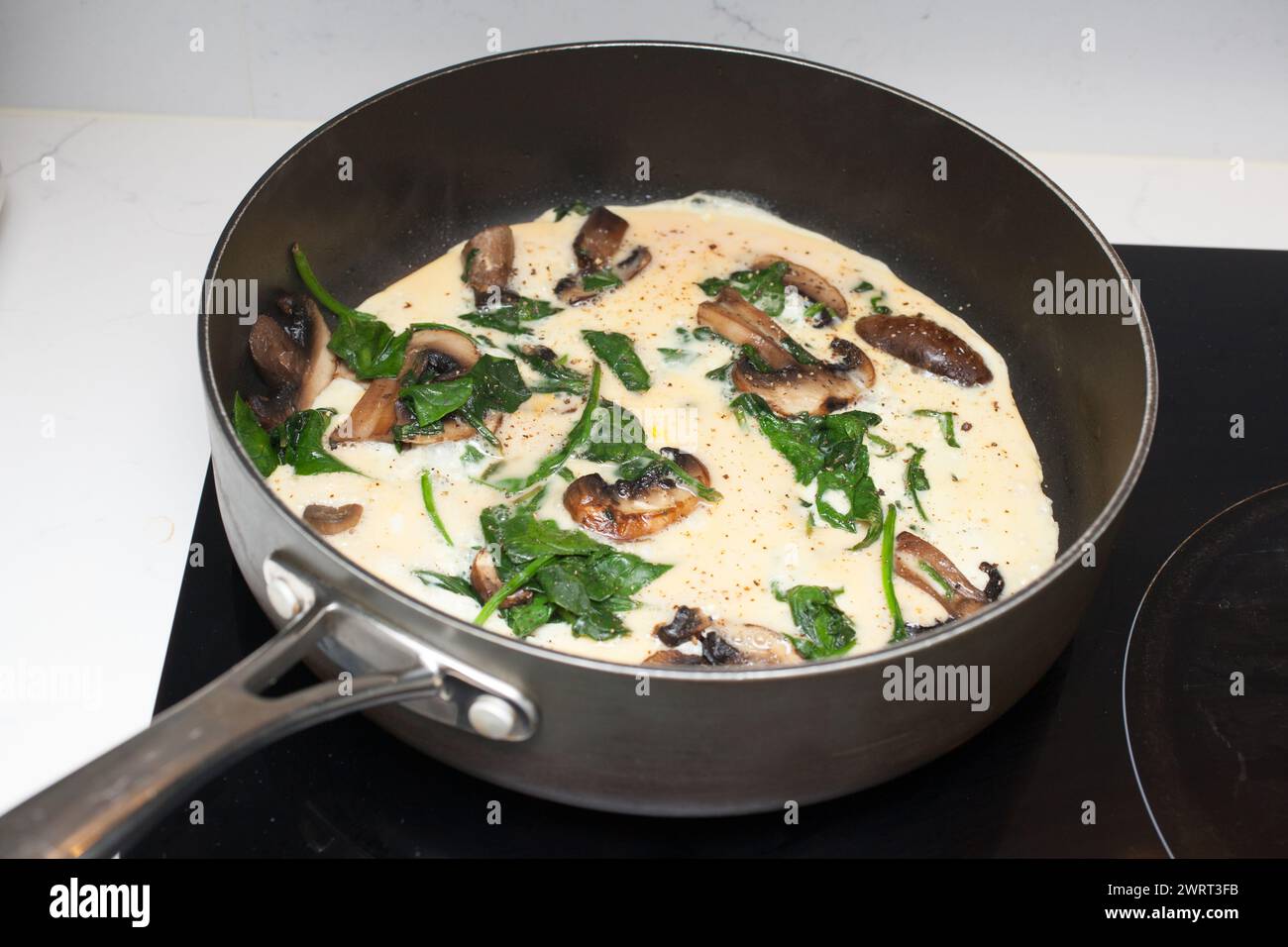 Une omelette aux épinards et aux champignons en cours de cuisson dans une poêle à frire Banque D'Images