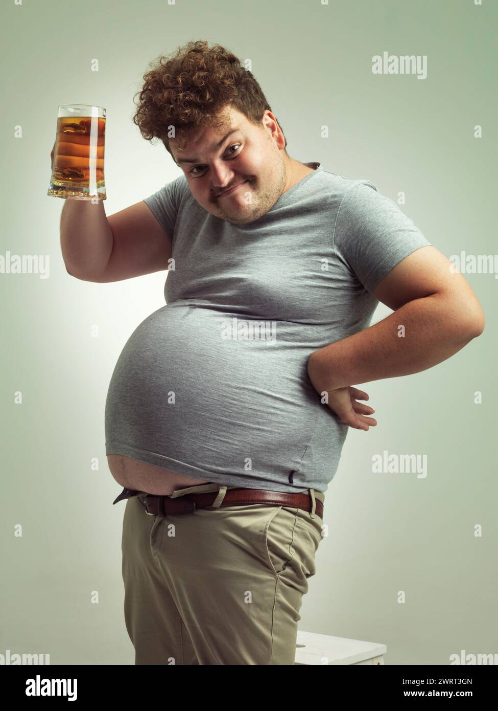 Obèse, gain de poids et bière pour homme en studio avec de l'alcool pour les habitudes malsaines, plus la taille et l'humour. Personne en surpoids avec verre à la main et graisse Banque D'Images