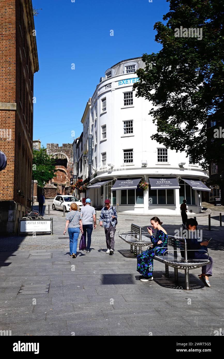 Les gens assis sur des bancs utilisant des téléphones mobiles avec vue le long de Castle Street vers le château de Rougemont, Exeter, Devon, Royaume-Uni, Europe. Banque D'Images