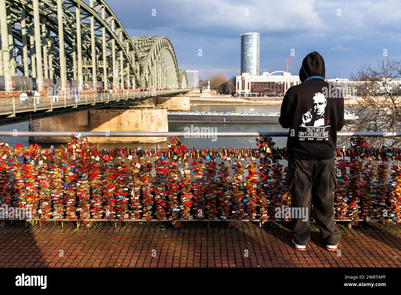 Homme avec sweat à capuche debout à la clôture avec les serrures d'amour au pont Hohenzollern, vue sur le Rhin jusqu'au gratte-ciel KoelnTriangle et le Hyatt Ho Banque D'Images
