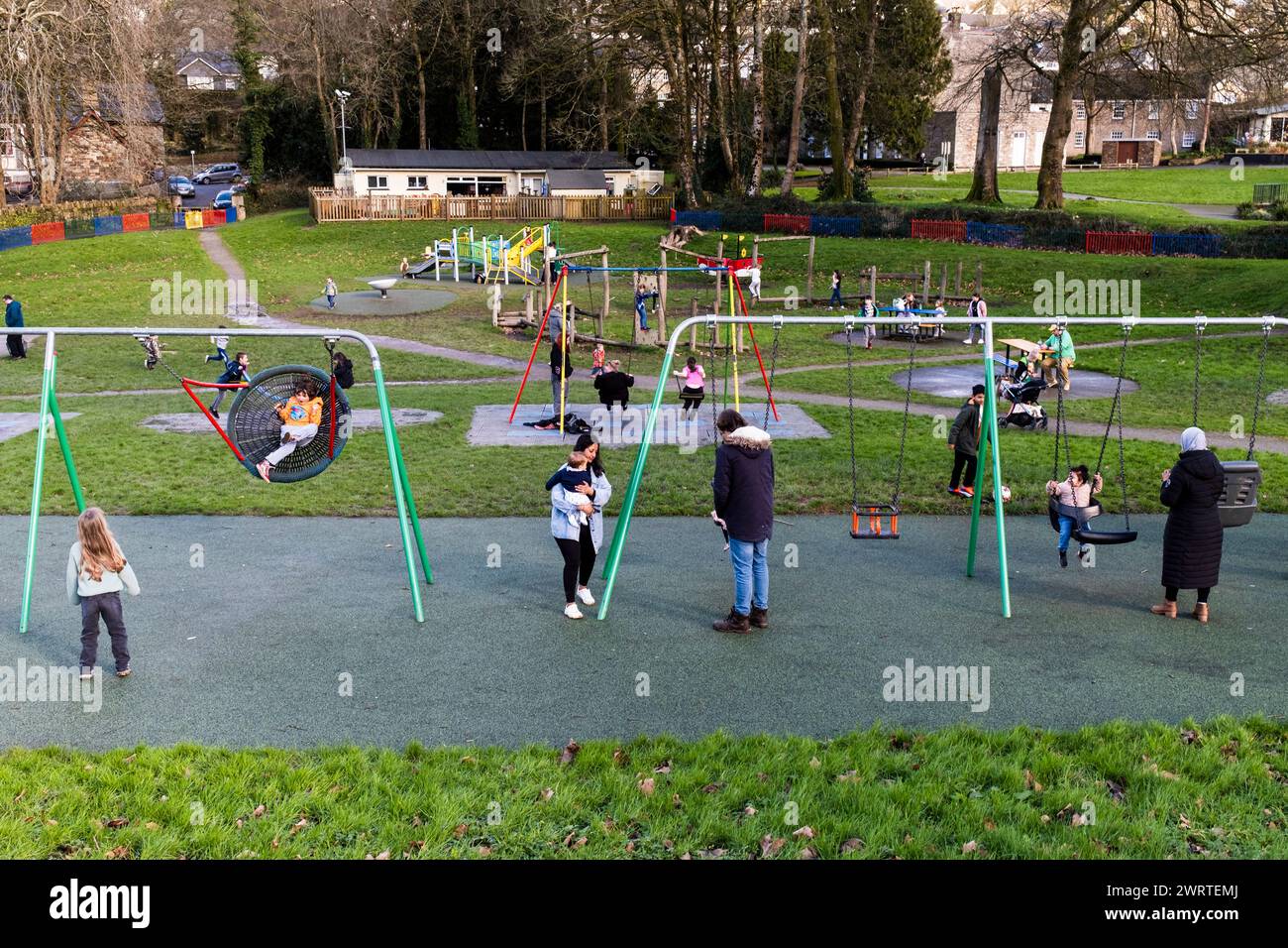 Parents et enfants jouant sur des balançoires dans le terrain de jeu Priory Park à Bodmin Town en Cornouailles au Royaume-Uni. Banque D'Images