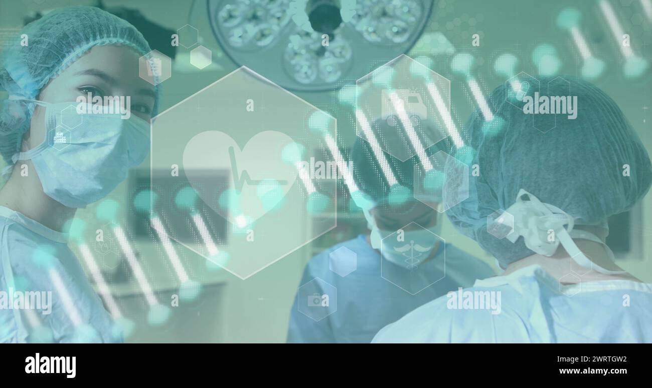 Image d'un brin d'ADN tournant et d'icônes médicales sur des chirurgiens portant des masques pendant un opérat Banque D'Images