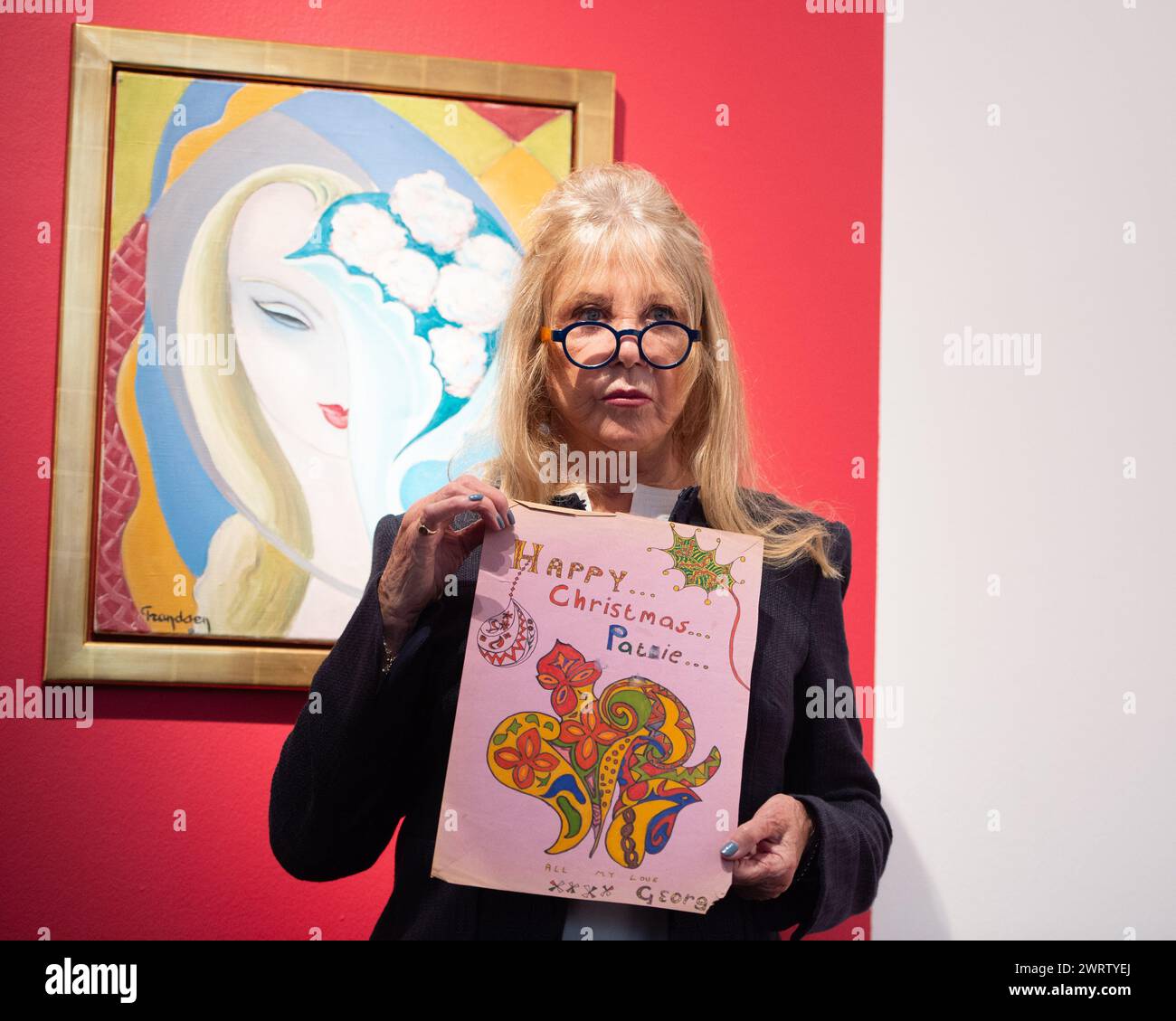 Londres, Angleterre, Royaume-Uni. 14 mars 2024. Modèle, photographe et icône PATTIE BOYD détient une œuvre de Noël exécutée par George Harrison pour son circa 1968. La pièce comporte de l'encre noire et des stylos feutres multicolores sur une feuille de papier mauve, mettant en valeur un motif floral et folié tourbillonnant avec un lettrage ornemental indiquant « HAPPY. Noël. Pattie.', à côté de l'inscription 'All My Love, XXXX George' dans l'écriture manuscrite de Harrison au verso, avec le message supplémentaire 'To Pattie, with Love from George, Christmas xx' (crédit image : © Thomas Krych/ZUMA Press Wire) USAGE ÉDITORIAL SEULEMENT! Non Banque D'Images