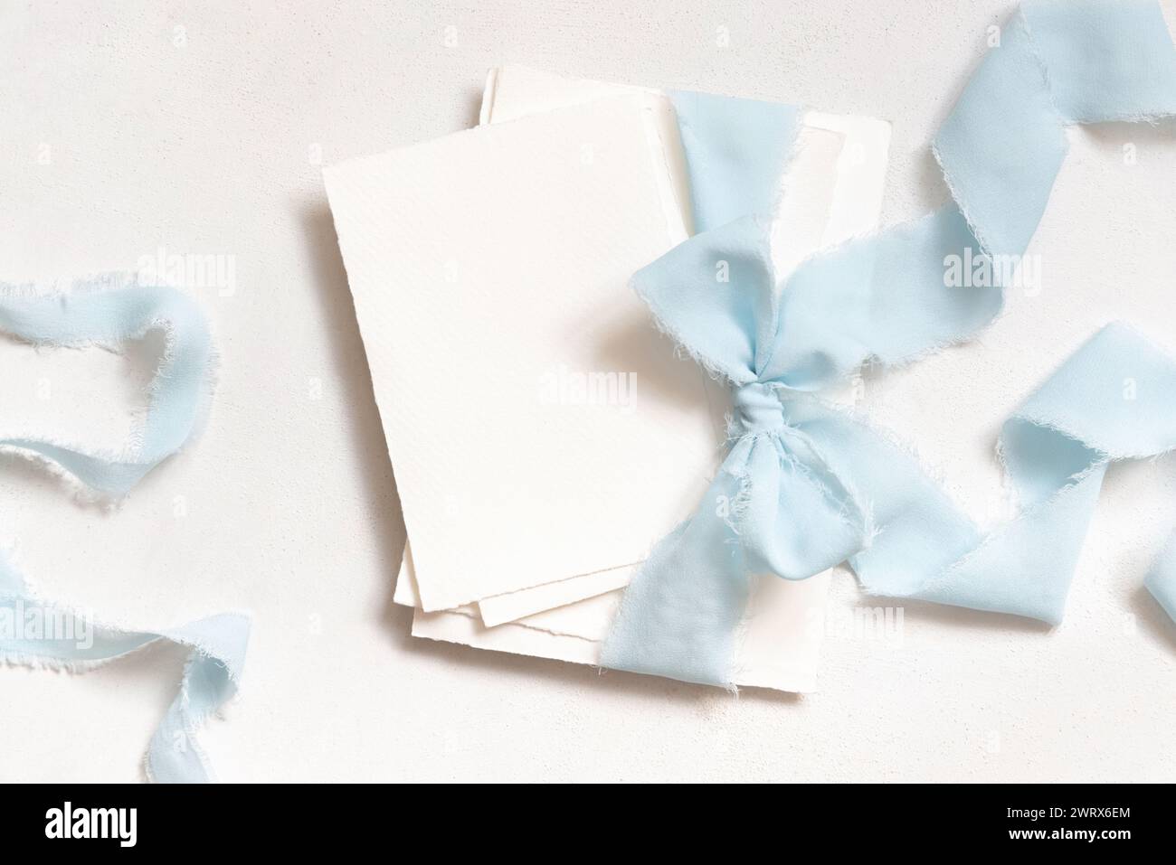 Cartes attachées avec un ruban de soie bleu clair sur la vue de dessus de table blanche. Maquette de papeterie de mariage. Scène romantique avec des cartes vierges verticales. Mariage, Valen Banque D'Images