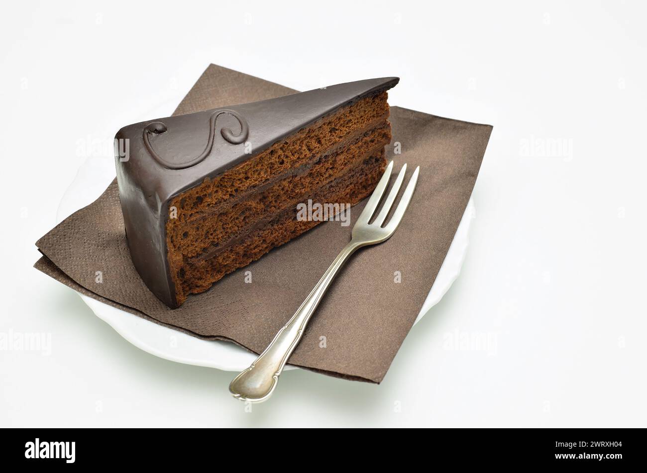 Morceau de torte Sacher sur plaque blanche, avec fourchette et serviette brune en gros plan, isolé sur fond blanc Banque D'Images