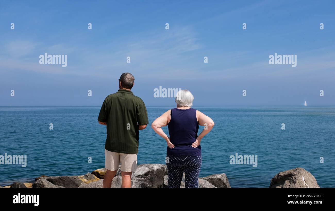 Couple aîné regarder sur les eaux bleues calmes du lac Ontario depuis la jetée de Port Dalhousie, équipée Catharines, Ontario, Canada. Banque D'Images