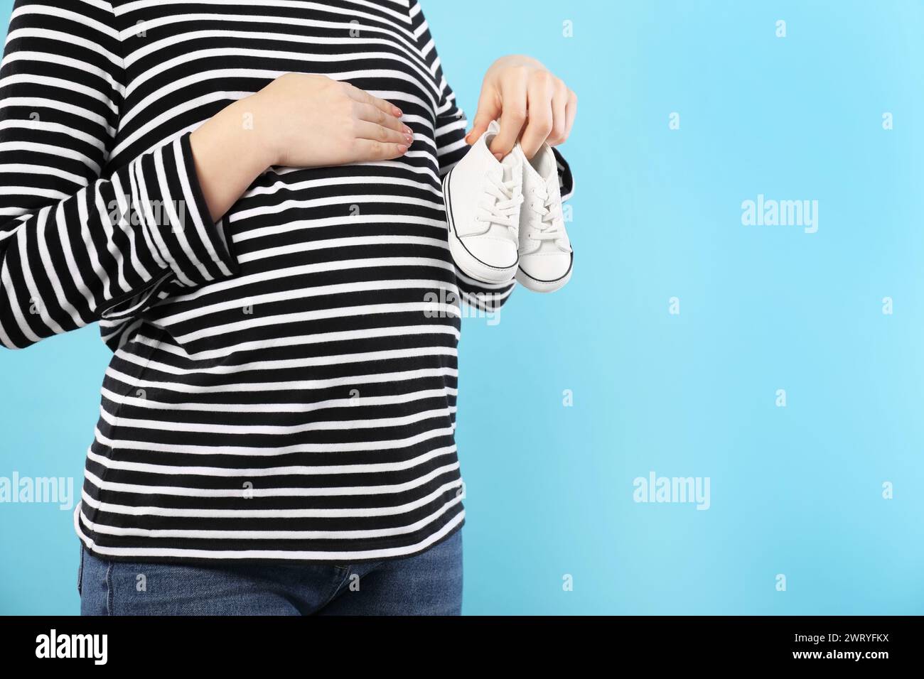 Femme enceinte avec des chaussures de bébé sur fond bleu clair, gros plan. Espace pour le texte Banque D'Images