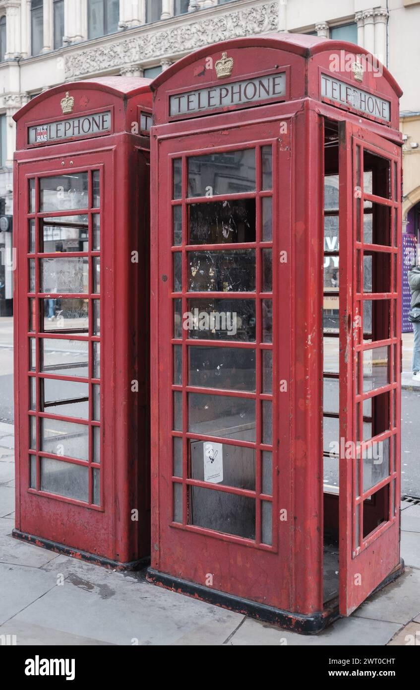 Deux cabines téléphoniques britanniques rouges traditionnelles côte à côte sur le trottoir de la ville avec verre brisé et manquant et peinture écaillée et usée. Door AJAR. Banque D'Images