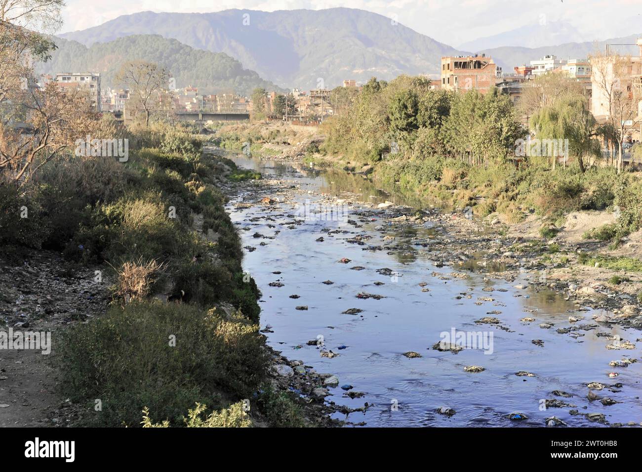 Une rivière avec des pierres coule à travers un paysage urbain avec une végétation verdoyante et des montagnes en arrière-plan, impressions du Népal, en voyageant à partir Banque D'Images Une rivière avec des pierres coule à travers un paysage urbain avec une végétation verdoyante et des montagnes en arrière-plan, impressions du Népal, en voyageant à partir Banque D'Images