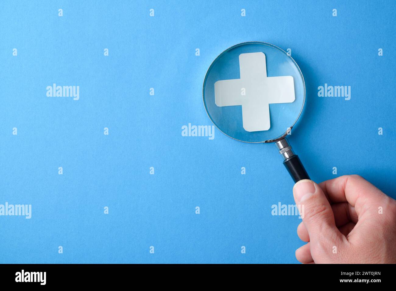 Information médicale et examen de fond avec la main grossissant une croix médicale avec une loupe et des lettres avec message de santé sur bleu est Banque D'Images