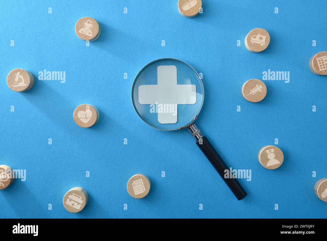 Concept de services médicaux et d'assurance avec loupe agrandissant la croix et les jetons en bois montrant différents services médicaux sur bac isolé bleu Banque D'Images