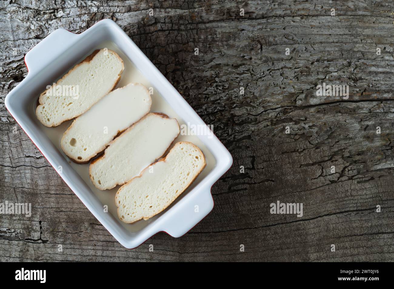 Tranches de pain trempées dans le lait pour faire des torrijas. Arrière-plan rustique en bois. Copier l'espace. Banque D'Images