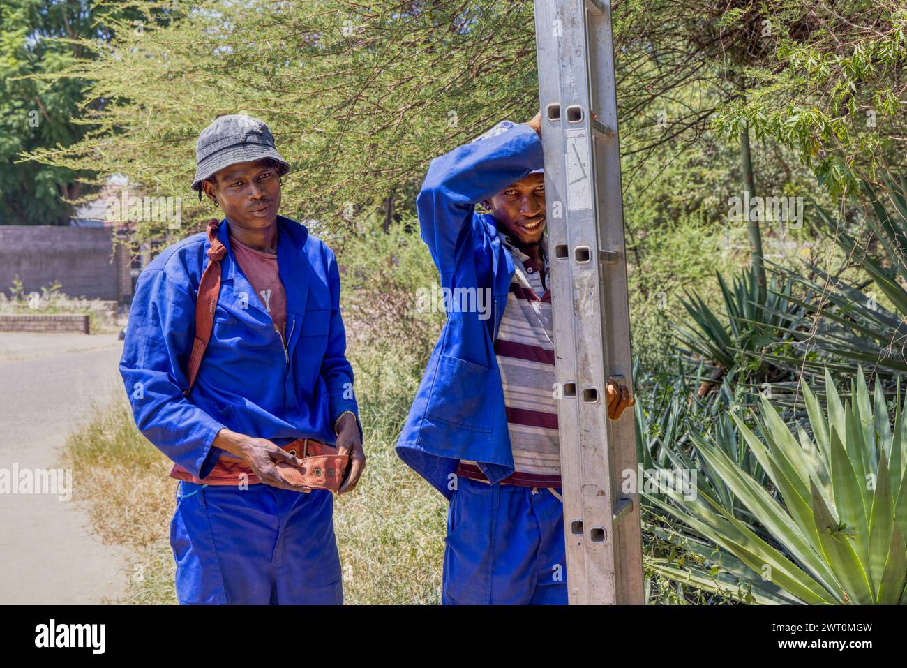 homme africain grimpant une échelle sur un poteau en bois pour fixer les lignes téléphoniques et les fils électriques Banque D'Images