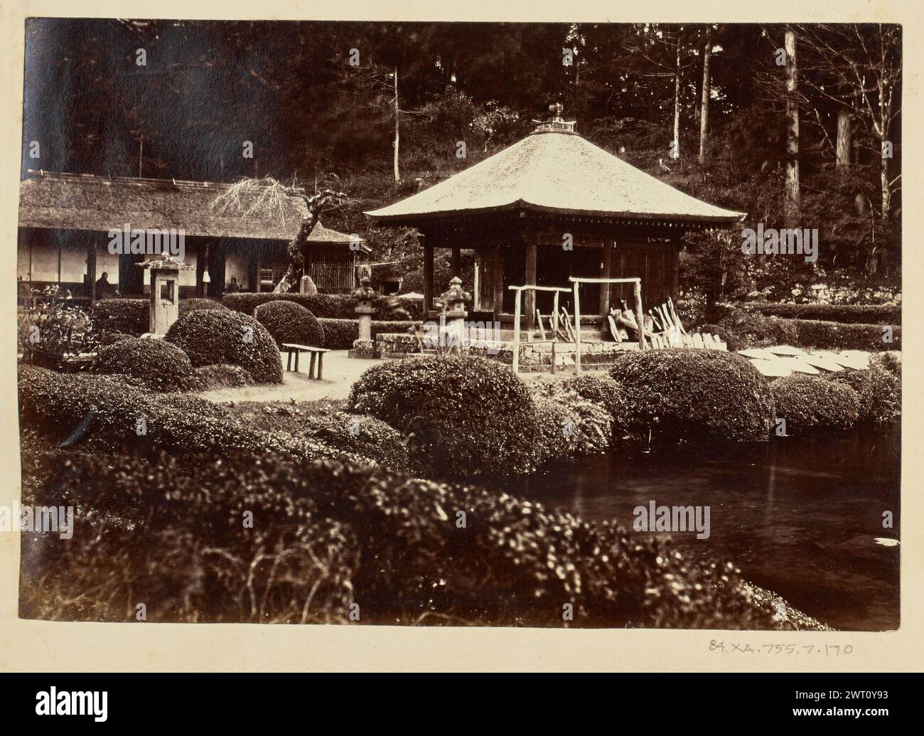 Jardin du temple. Inconnu, photographe des années 1850–1890 vue à l'intérieur du jardin d'un complexe de temples japonais non identifié. Des arbustes soigneusement taillés bordent un étang et des sentiers qui serpentent à travers le jardin. Bancs, tachidoro, ou lanternes sur piédestal, et petits sanctuaires sont dispersés partout. Deux personnages peuvent être vus assis sur des bancs sur le porche d'un bâtiment de temple plus petit. Banque D'Images