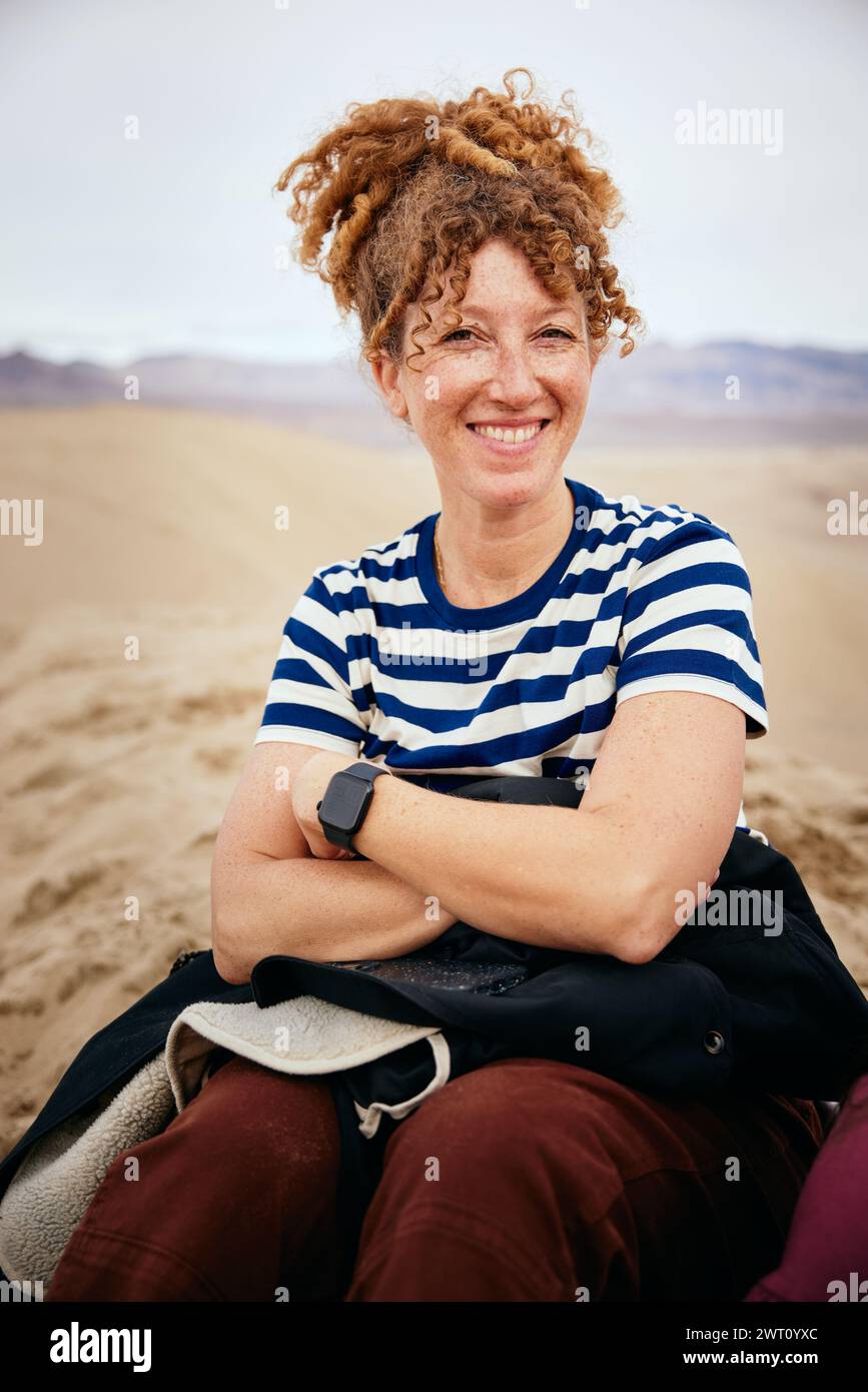 Femme souriante assise avec les bras croisés sur le sable à Death Valley Banque D'Images