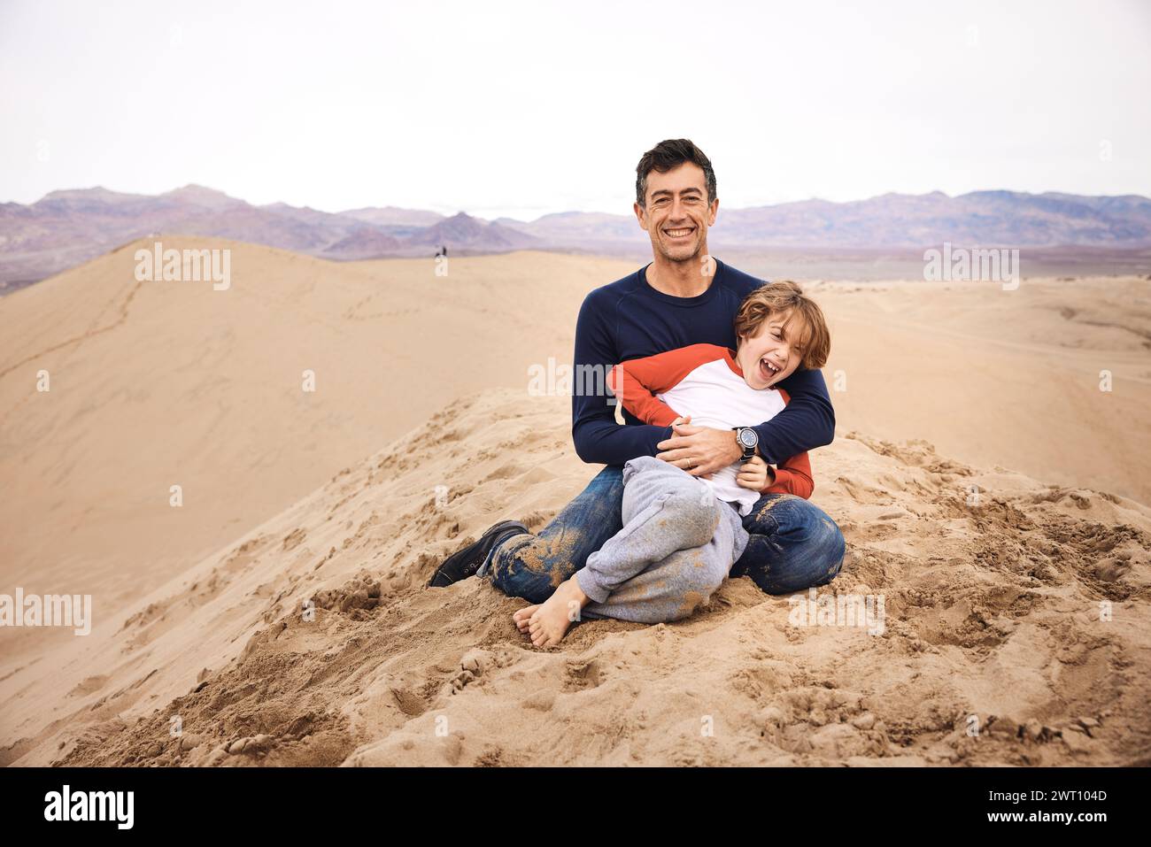 Portrait d'homme heureux jouant avec son fils assis sur une dune de sable Banque D'Images