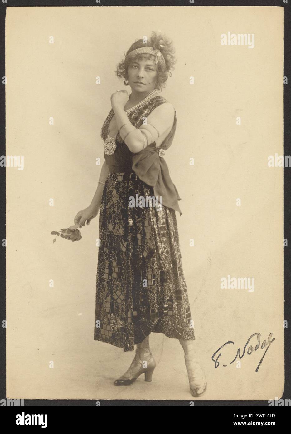 Mlle polaire. Paul Nadar, photographe (français, 1856 - 1939) vers 1910 Portrait en pied de l'actrice Émilie Marie Bouchaud, connue sous le nom de scène polaire. Elle porte un double brin de grosses perles autour de son cou et une broche perle épinglée à la taille de sa robe coupe basse. Elle pose avec une jambe tendue derrière elle et son pied pointu, et tient un bras vers le haut près de son menton. Elle tient un petit bouquet de fleurs dans son autre main. (Verso, impression) manuscrite au crayon : 'Mlle polaire / 21768' Banque D'Images