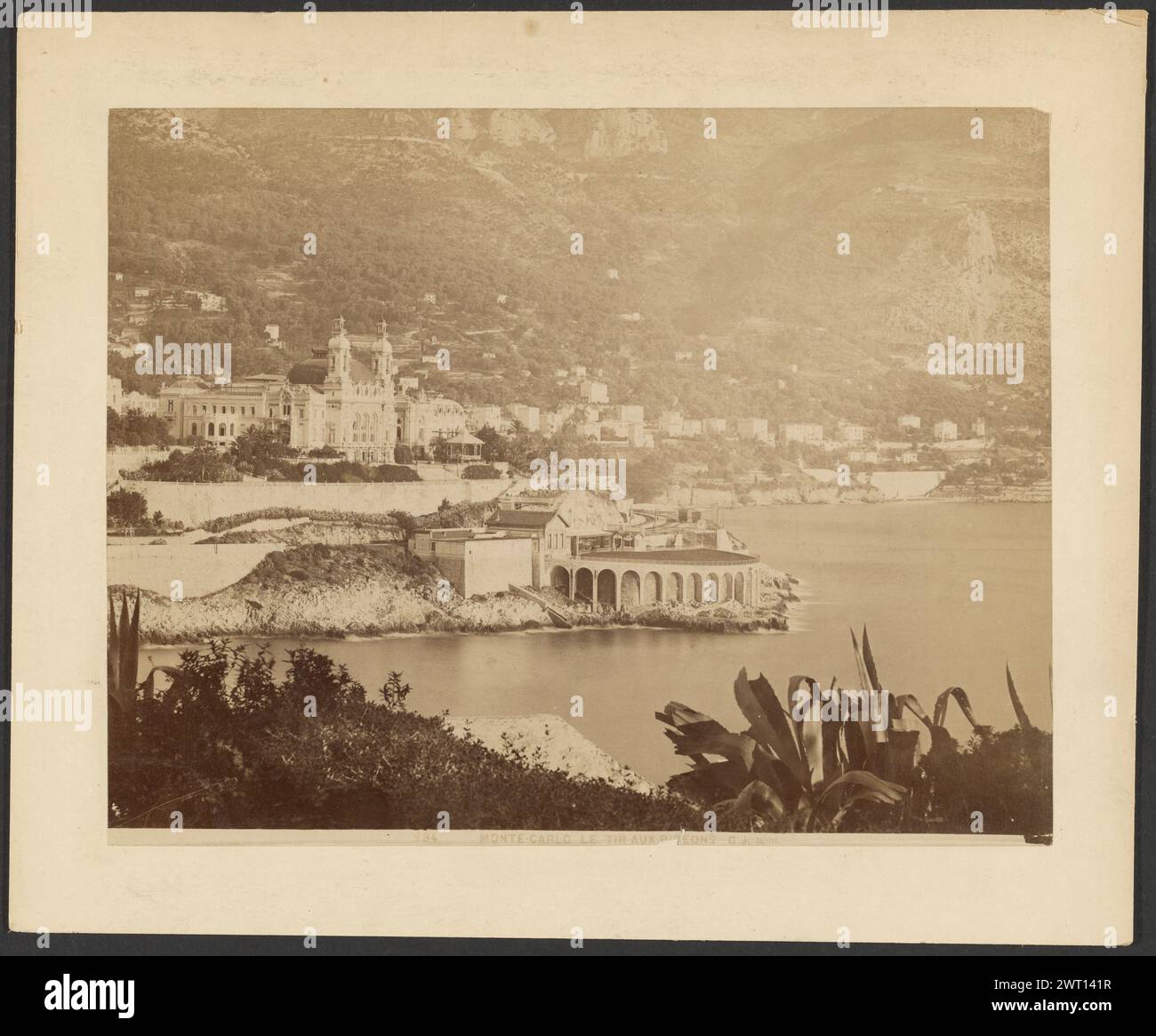Monte Carlo, le tir aux pigeons. G. J., photographe (français, actif années 1870 - années 1880) 1870–1880 vue du Casino de Monte Carlo et des collines qui l'entourent depuis l'autre côté de l'eau. Le casino est vu de côté à un angle et il y a du feuillage au premier plan. Banque D'Images