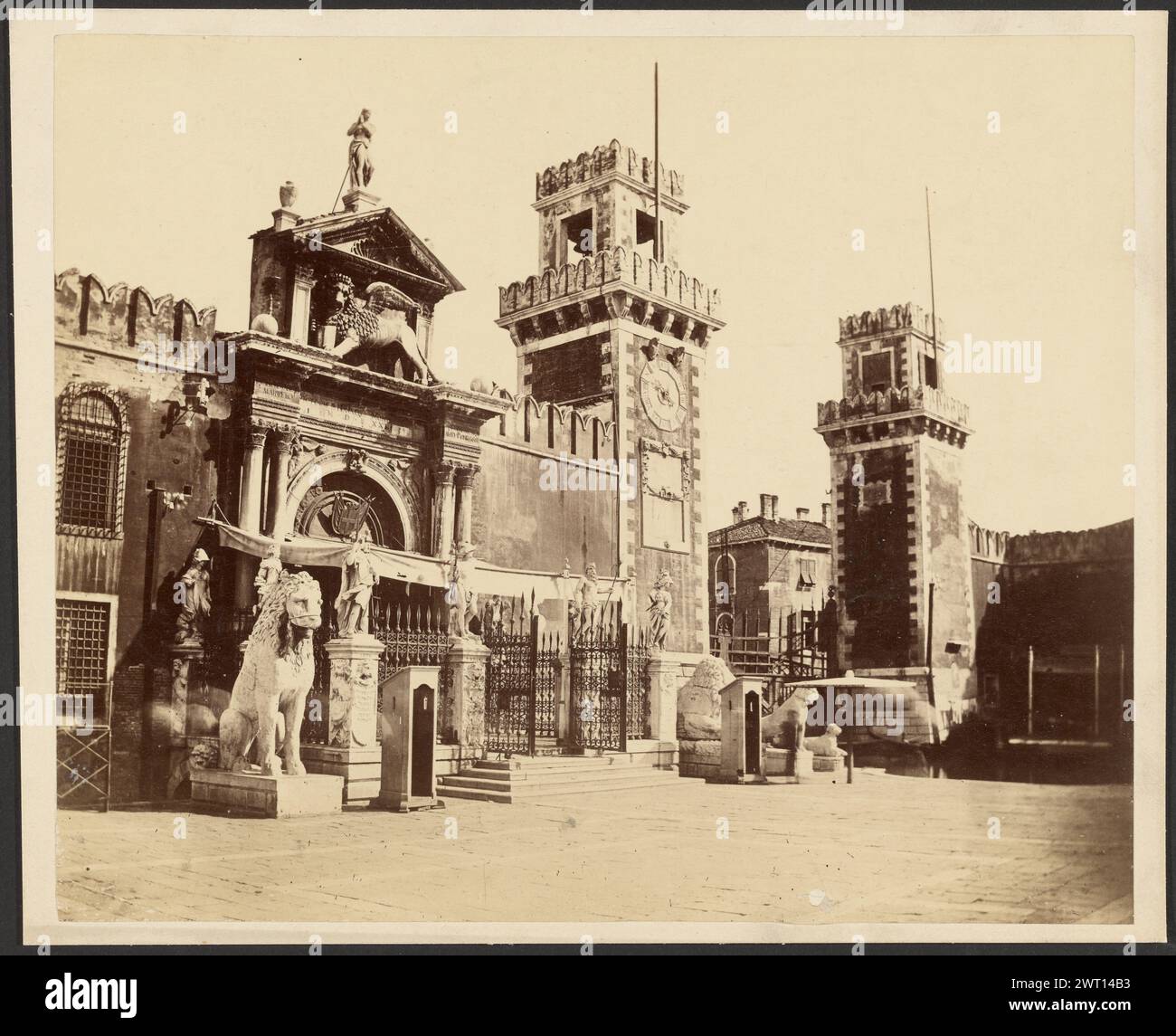 Arsenal vénitien. Inconnu, photographe vers 1860–1880 vue inclinée de la porte principale de l'arsenal vénitien. L'entrée est fermée par une clôture en fer forgé avec un lion en pierre assis sur un côté. Des piédestaux avec de petites statues de figures sont placés le long de la clôture. Une statue de lion ailée est sur le rebord au-dessus de l'entrée de l'arensal. Le bâtiment a une tour de l'horloge avec une cloche au coin le plus éloigné. (Verso, monture) en haut à gauche, encre noire : 'marathon' ; au centre, crayon : 'Arsenal-Enice/Lion of Marathon'; Banque D'Images