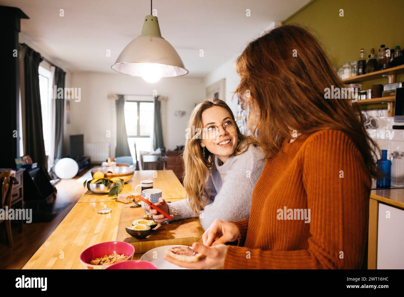 Un couple de lesbiennes préparant le petit déjeuner et partageant un moment intime ensemble, dans l'atmosphère chaleureuse de leur cuisine à la maison. Banque D'Images