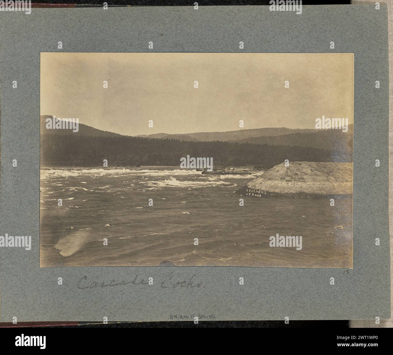 Serrures en cascade. J.F. Ford, photographe (américain, actif dans les années 1900) vers 1900 vue des rapides des Cascades sur le fleuve Columbia. Un mur de pierre artificiel s'étend à partir de l'écluse de cascade, non visible dans le cadre. Les arbres à feuilles persistantes recouvrent le paysage en arrière-plan. (Recto, monture) centre inférieur, en dessous de l'impression, manuscrit à l'encre noire : 'Cascade Locks' en bas à droite, en dessous du coin droit de l'impression, manuscrit à l'encre noire : '15' Banque D'Images