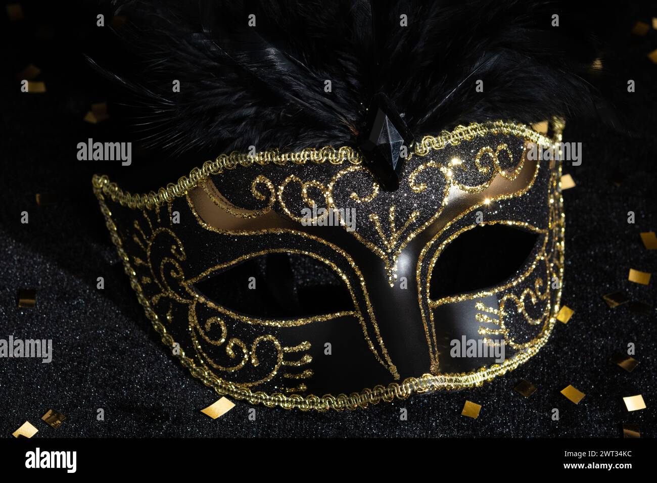 Masque d'or mascarade avec des plumes et des confetties sur fond noir. Banque D'Images