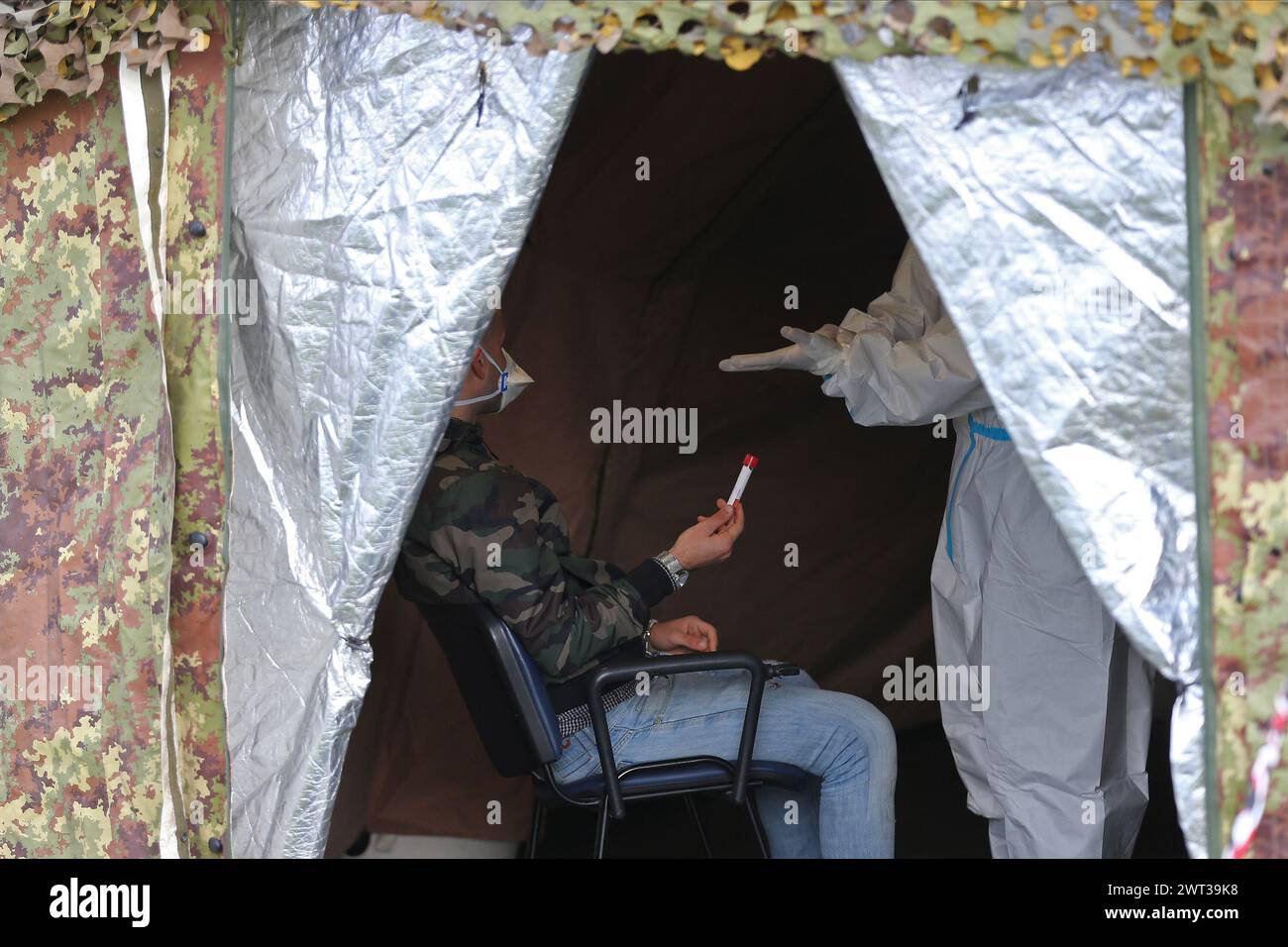 Un homme, devant un médecin, tient un tube à essai dans sa main avant de prélever un écouvillon, dans la tente du camp militaire installée à l’hôpital Frullone à Naple Banque D'Images