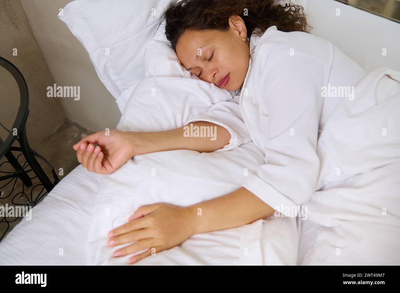 Vue aérienne d'une jeune femme adulte multi ethnique dormant. Vue en angle élevé de belle jeune femme en pyjama blanc, couchée dans le lit et gardant son EY Banque D'Images