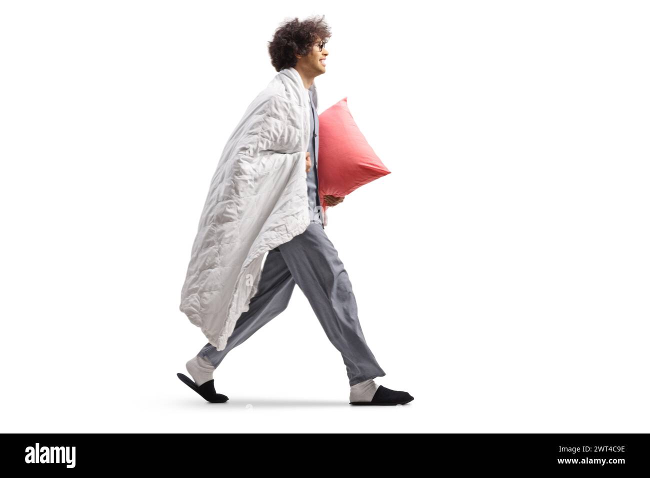 Jeune homme en pyjama enveloppé dans une couverture portant un oreiller et marchant isolé sur fond blanc Banque D'Images