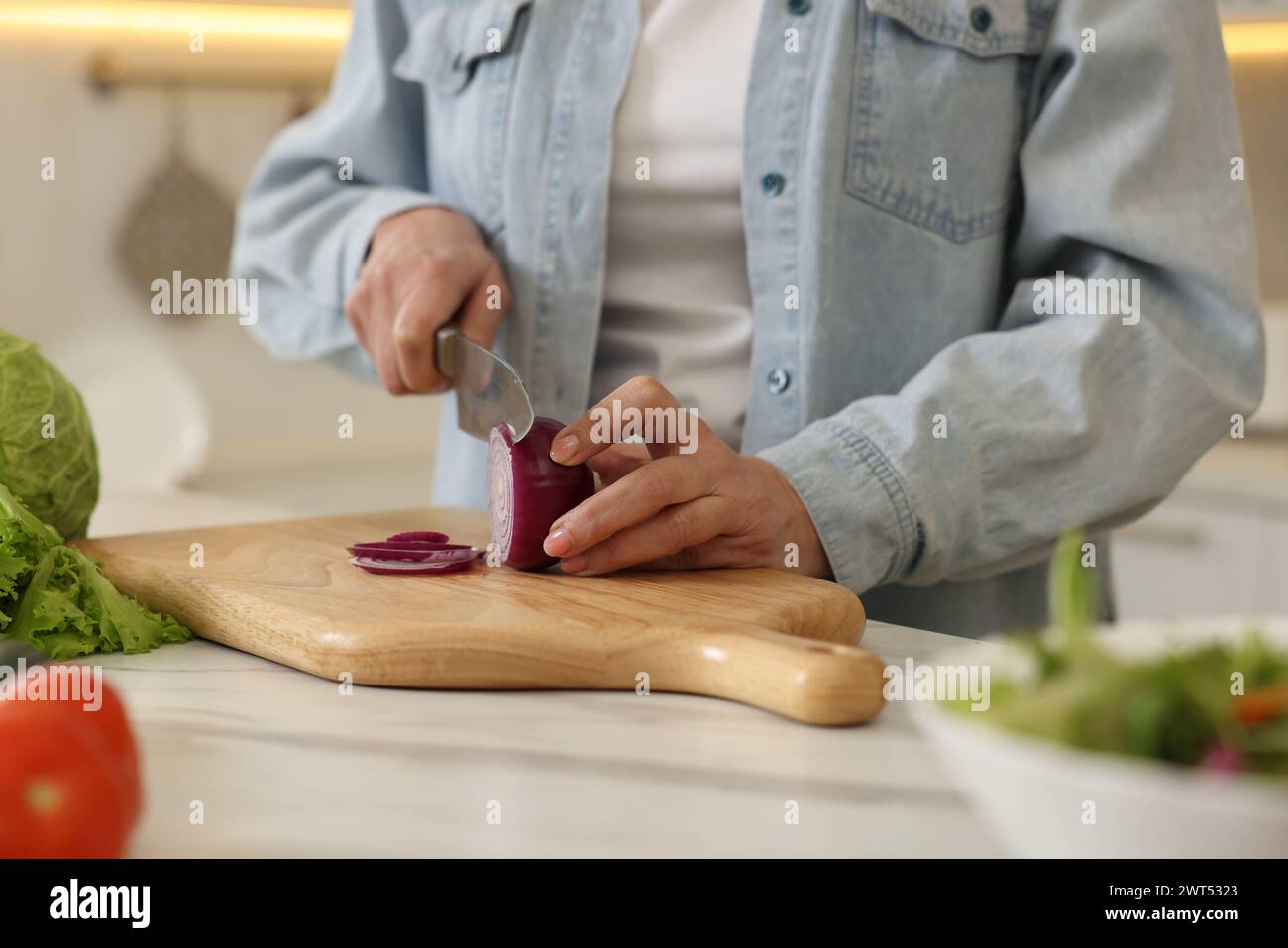 Femme coupant l'oignon à la table en marbre blanc dans la cuisine, gros plan Banque D'Images