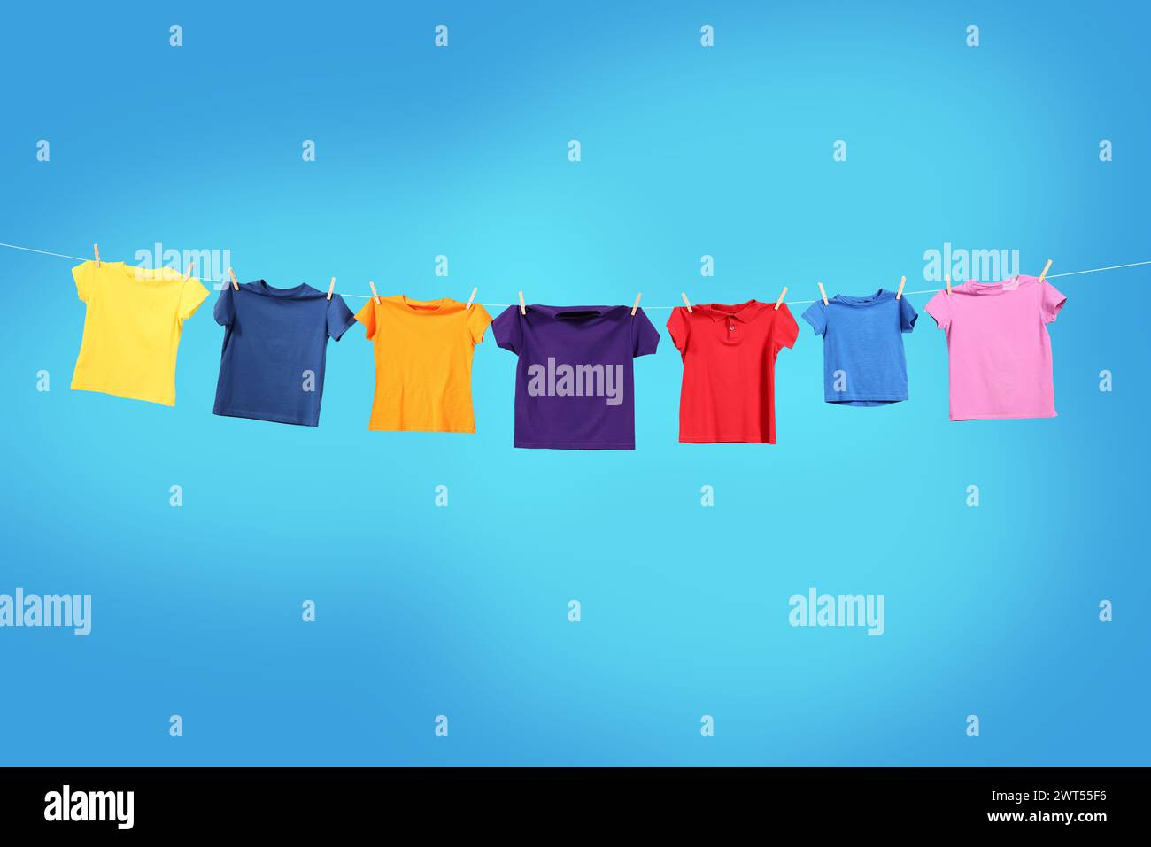 T-shirts colorés séchant sur la ligne de lavage sur fond bleu clair Banque D'Images T-shirts colorés séchant sur la ligne de lavage sur fond bleu clair Banque D'Images